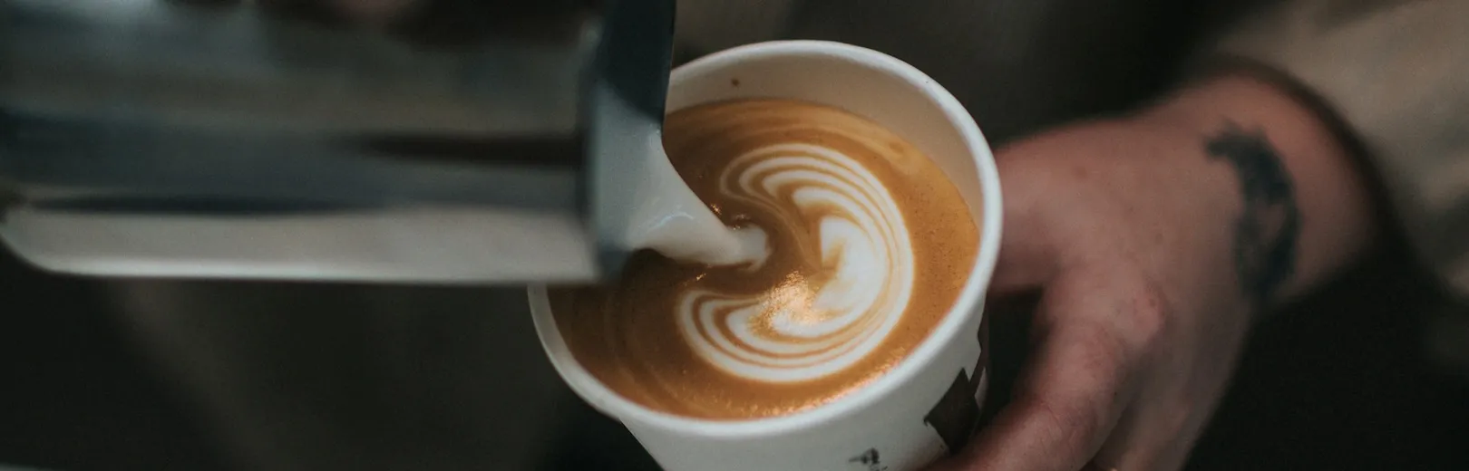 A barista pours latte art in a takeaway coffee cup.