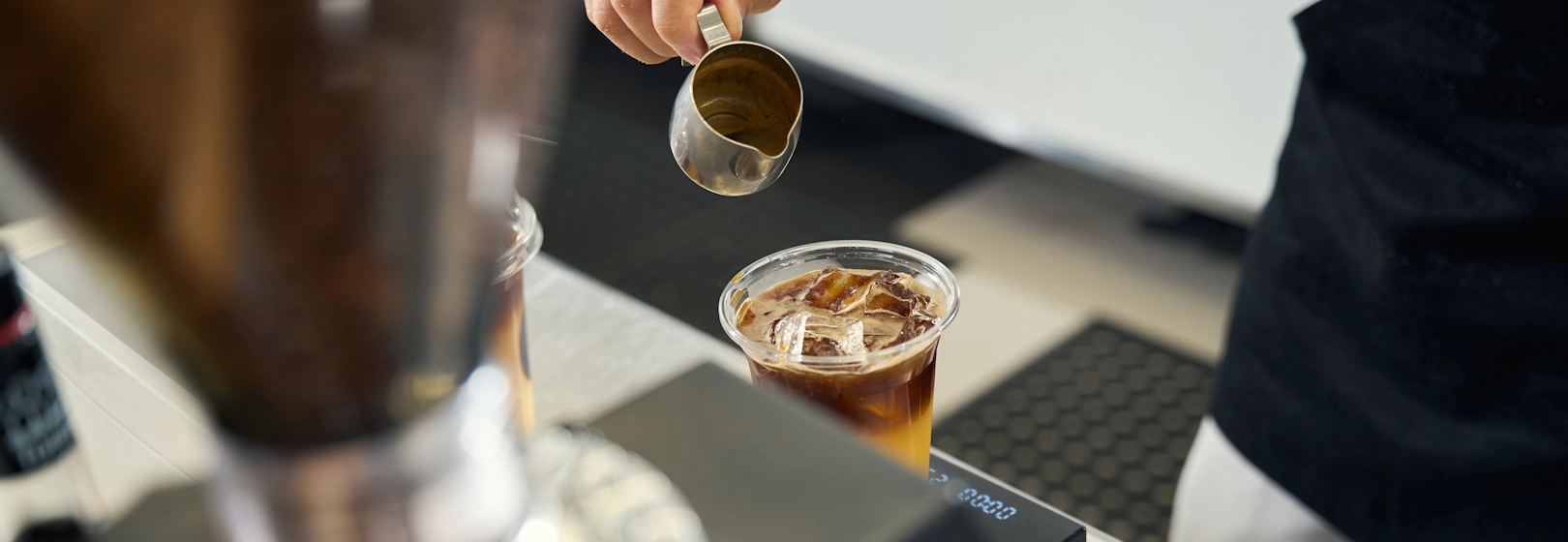 Barista pours espresso into a plastic takeaway cup.